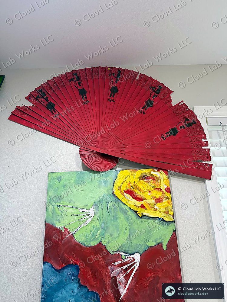 A red lacquer folding fan with silhouette figures resting on the top edge of an acrylic canvas