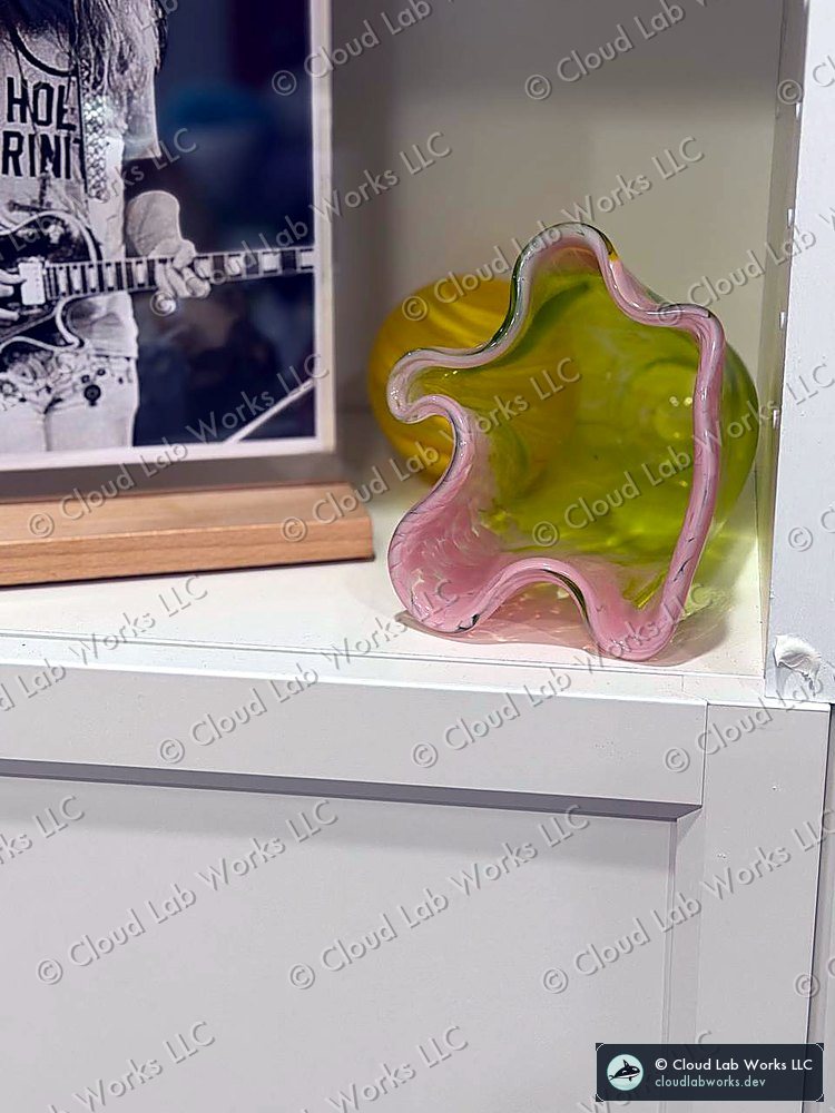 Hand-blown glass bowl with a ruffled pink rim over a yellow-green body, on a shelf